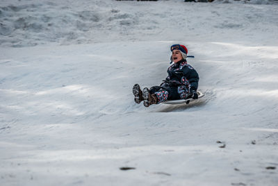 Cheerful boy tobogganing on snow