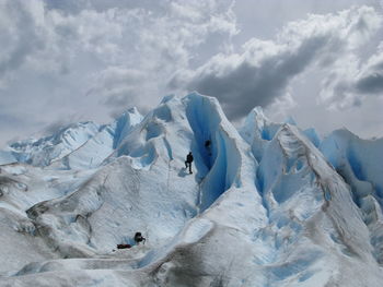 Scenic view of snowcapped mountains against sky and two people escalating them. 