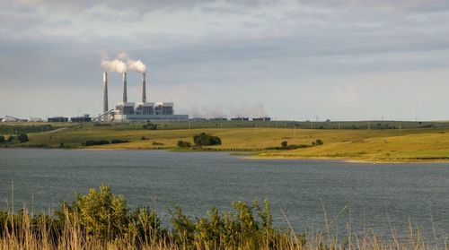 Built factory structure in field by lake against sky