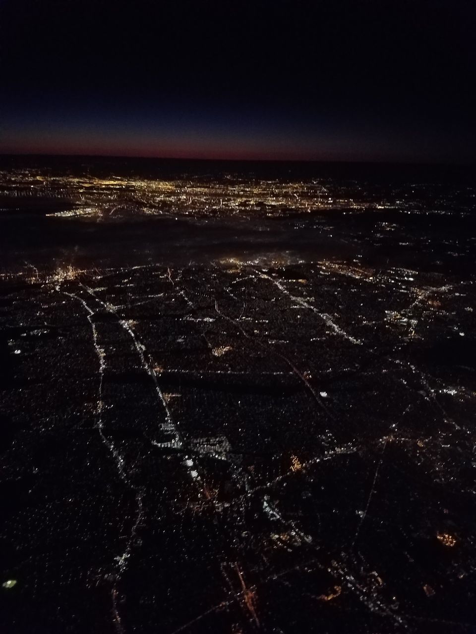 AERIAL VIEW OF ILLUMINATED CITY BY SEA AT NIGHT
