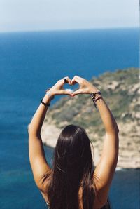 Rear view of woman making heart shape against sea