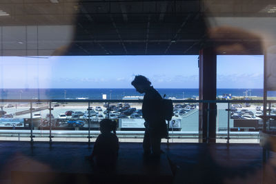 Silhouette woman standing by window against sky