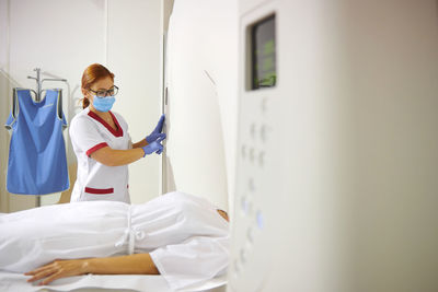 Doctor in uniform and eyeglasses using tomography machine with lying female patient in hospital