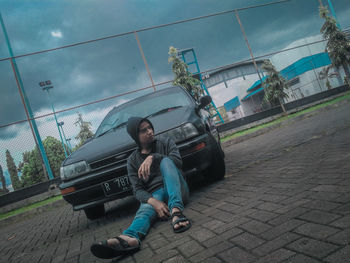 Boy sitting on footpath against sky