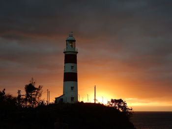 Lighthouse by sea against sky during sunset