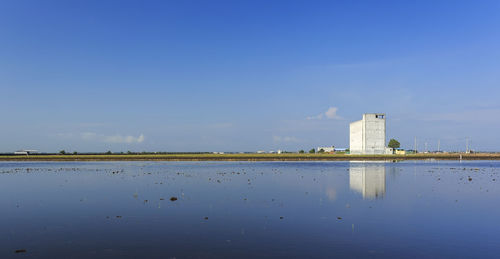 White building reflection in lake against blue sky