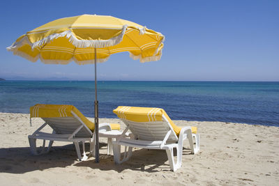 Deck chairs on beach against clear blue sky