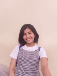 Portrait of smiling teenage girl standing against wall