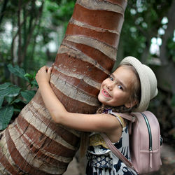 Cute girl embracing tree trunk in forest