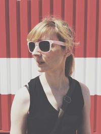 Woman wearing sunglasses while looking away against corrugated iron during sunny day