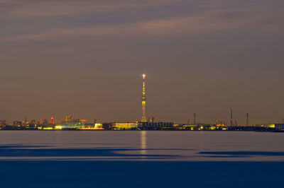 Illuminated city by sea against sky at night