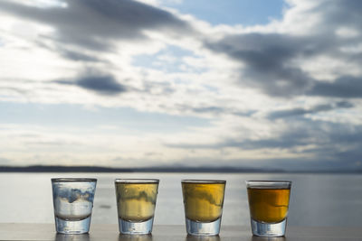 Tequila shots on table by sea against sky