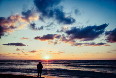 Silhouette person looking at sea against sky during sunset