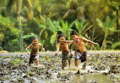 Shirtless boys running in muddy water