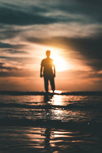 Silhouette man standing in sea against sky during sunset