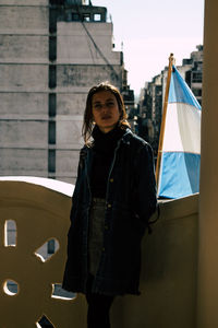 Portrait of young woman standing against building