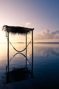 Silhouette wooden post in lake against sky during sunset