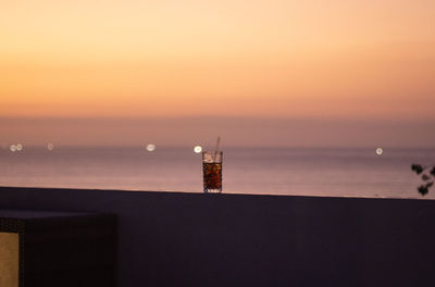 Silhouette building by sea against orange sky