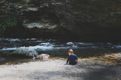 Rear view of baby boy sitting against lake at forest