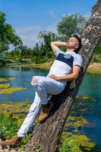 Side view of man sitting on tree trunk by lake