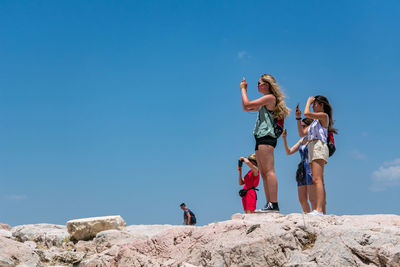 Low angle view of people on rock against clear blue sky