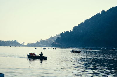 People in boat sailing on river against clear sky