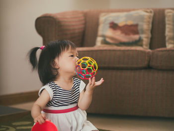 Cute girl biting toy while sitting at home