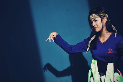 Young woman in traditional clothing dancing against wall