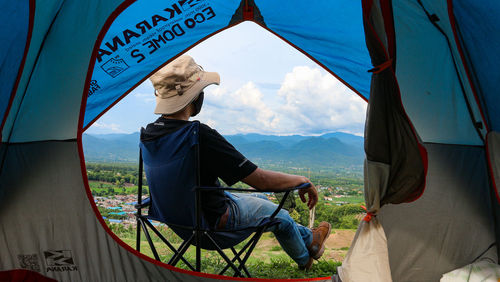 Rear view of man sitting at tent against sky