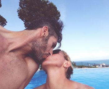 Young couple kissing in swimming pool against sky
