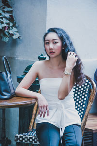 Portrait of young woman sitting at sidewalk cafe in city