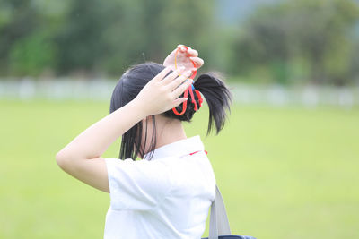 Young woman standing in park while tying pony tail