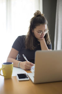 Young woman using phone while sitting on table