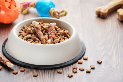 A bowl with dog food, dog treats and toys on a wooden floor. concept of healthy food for dogs.