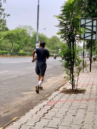 Full length rear view of man jumping on footpath