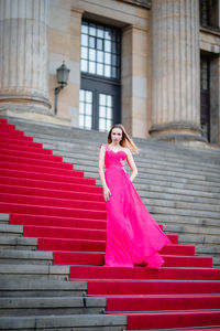 Female model wearing pink evening gown while standing on steps