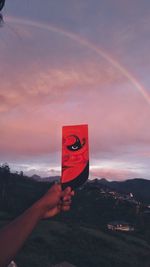 Person holding red umbrella against sky during sunset