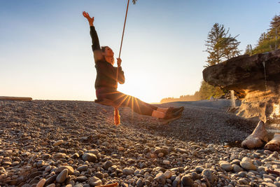 Man on rock at beach against sky during sunset