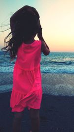 Rear view of woman standing on beach against sky during sunset