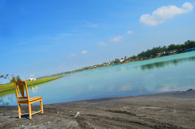 Empty chairs by swimming pool against sky