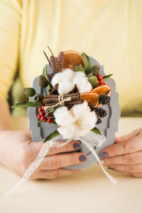 Woman holds bouquet with cotton flowers cinnamon and orange slices above table