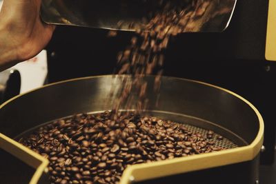 Cropped hand of worker pouring roasted coffee beans on strainer