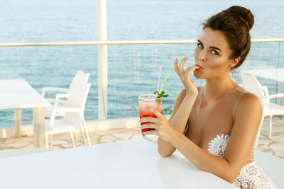 Beautiful woman drinking cocktail at restaurant against sea