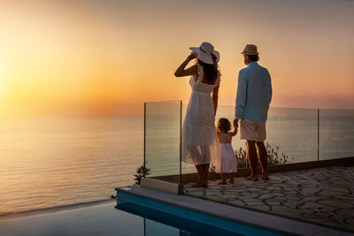 Rear view of family standing against sky during sunset