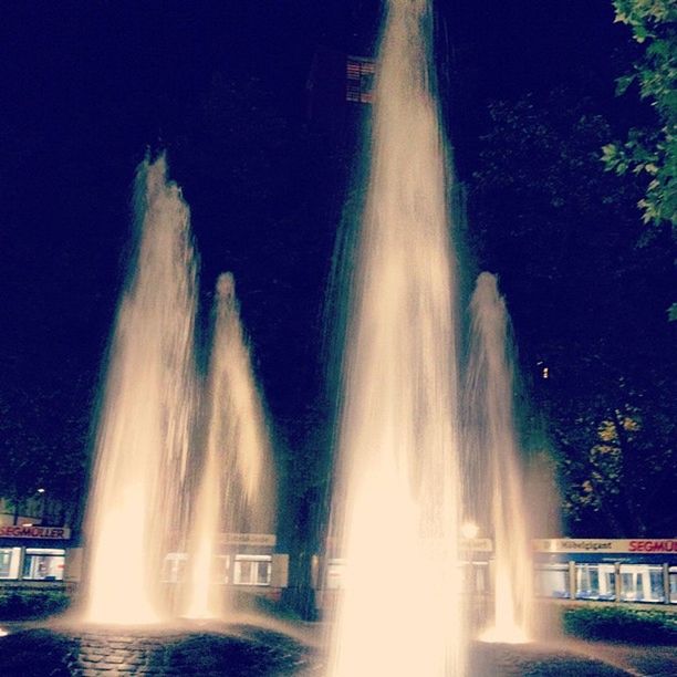 motion, long exposure, water, fountain, waterfall, spraying, flowing water, splashing, blurred motion, power in nature, tree, built structure, night, flowing, waterfront, speed, architecture, building exterior, famous place, low angle view