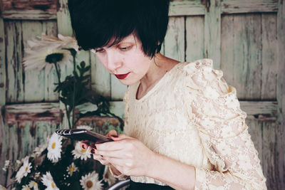 Close-up of woman using mobile phone against wooden wall