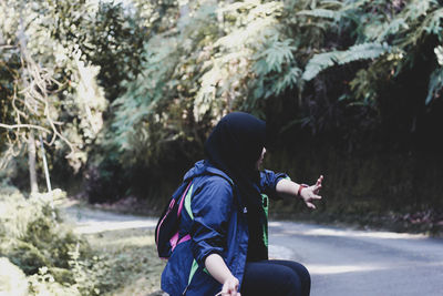 Side view of woman wearing hijab sitting by road in forest