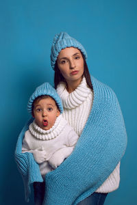 Mother and son in white sweaters and blue hats stand on a blue background in the studio