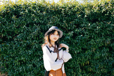 Portrait of young woman standing against plants