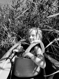 Portrait of smiling girl sitting on kayak by plants